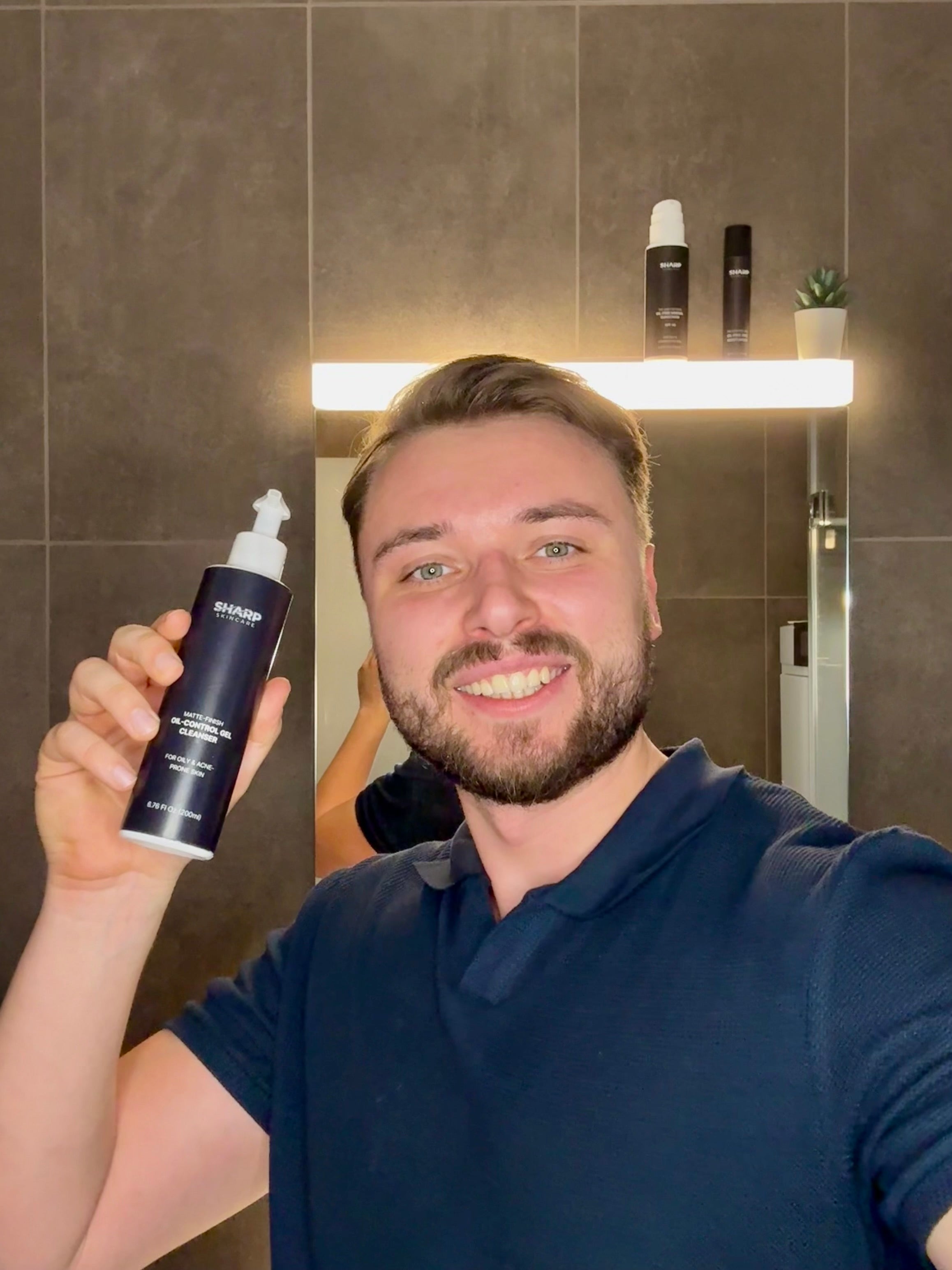 Founder Igor holding Sharp Skincare cleanser in front of a mirror in a bathroom.